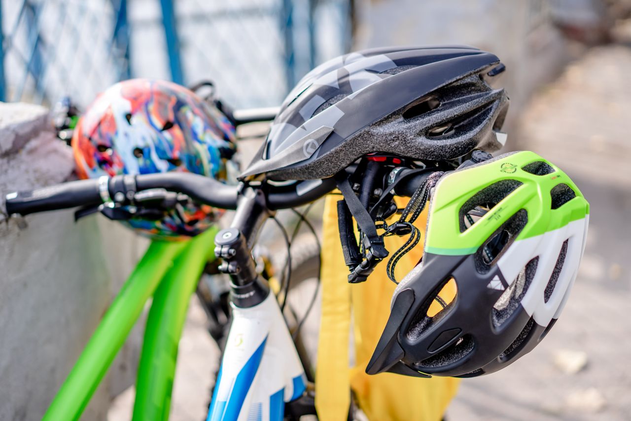 pexels-photo-12956080 Close-up of brightly colored bicycle helmets resting on bike handlebars, emphasizing safety.